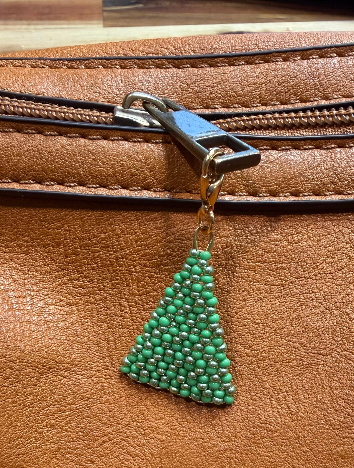 Christmas Pine handmade zipper pull by Amelia Heir Art, featuring green and metallic green beads in a pine tree shape attached to a brown leather bag’s zipper.