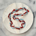 Americana Collection, 250 Anniversary, Three strand braided beaded necklace with red, white, and blue beads on a marble surface, gold stars and numbers 250, Amelia Heir Art