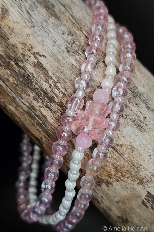 Beaded bracelets in pink and white and gummy-bear bead on a wooden surface