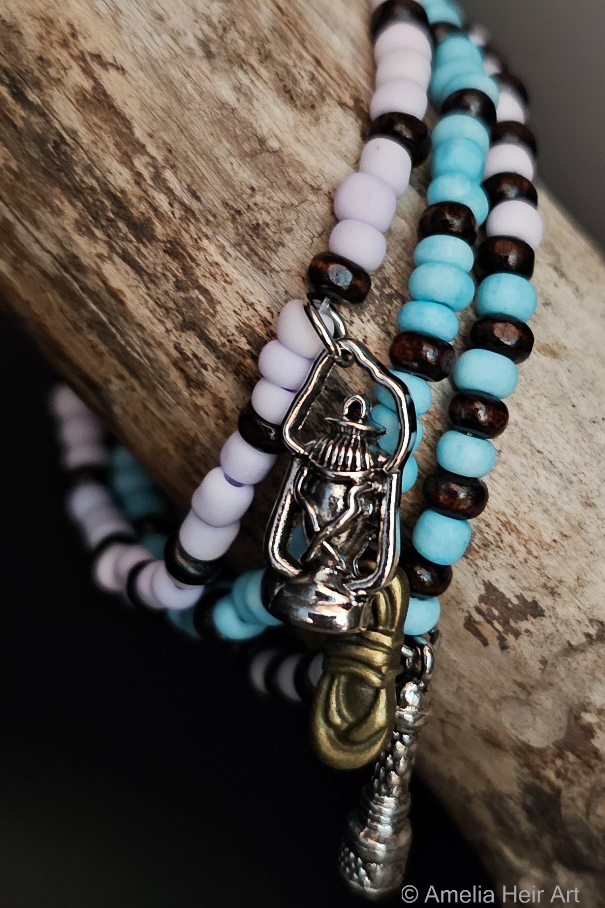 Set of beaded bracelets with silver lantern, gold rope, and silver telescope charms on a wooden surface