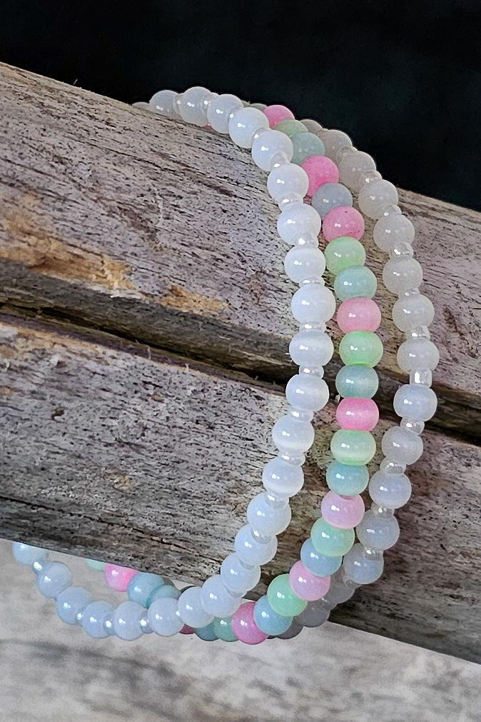 Set of three beaded bracelets in white and pastel colors on a wooden surface