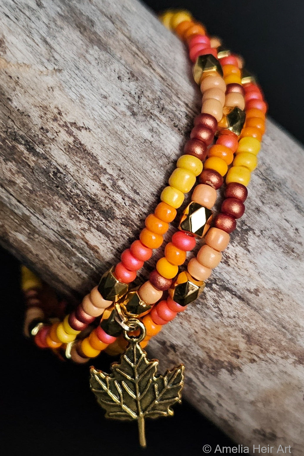 Stack of beaded bracelets with a gold leaf charm on a wooden surface