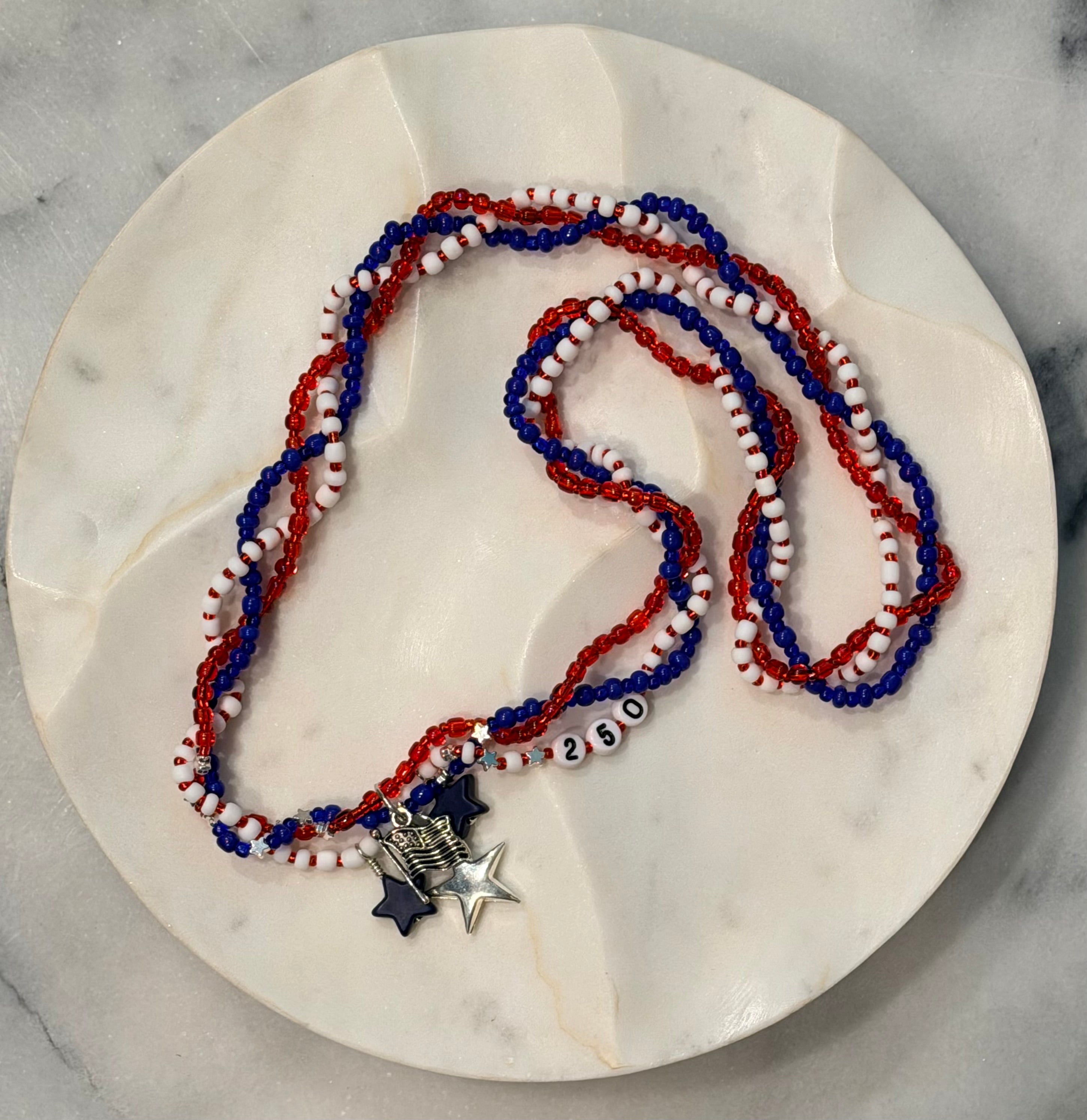 Allegiance 250 handcrafted braided necklace with navy star, silver flag & star charms and 250 beads on a marble surface — Amelia Heir Art