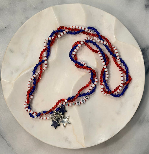 Allegiance 250 handcrafted braided necklace with navy star, silver flag & star charms and 250 beads on a marble surface — Amelia Heir Art