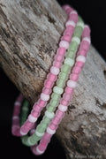 Three beaded bracelets in pink, green, and white glow-in-the-dark  beads on a wooden surface.