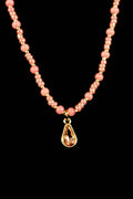 Necklace with pink beads and a gold teardrop pendant on a black background