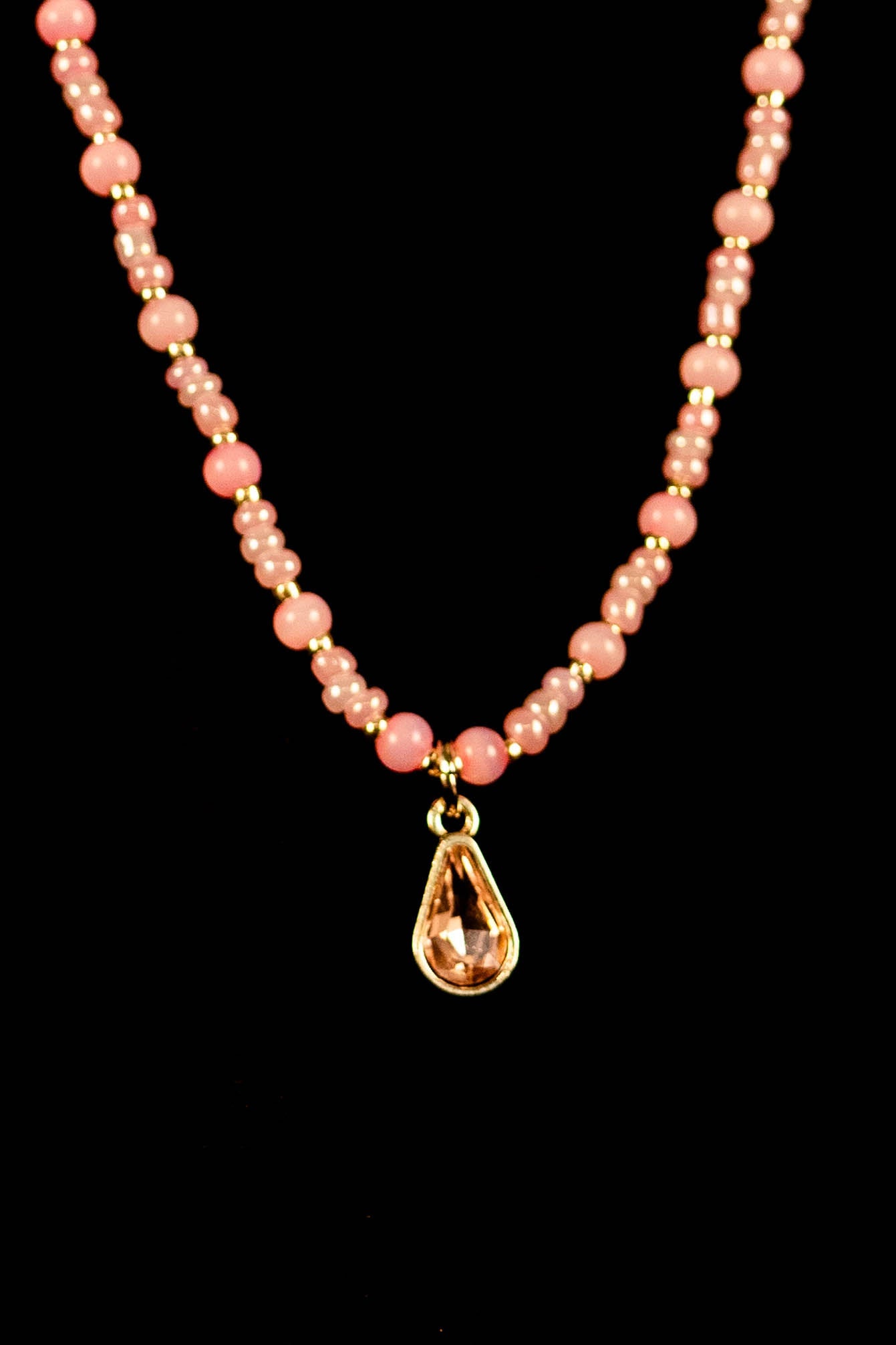 Necklace with pink beads and a gold teardrop pendant on a black background