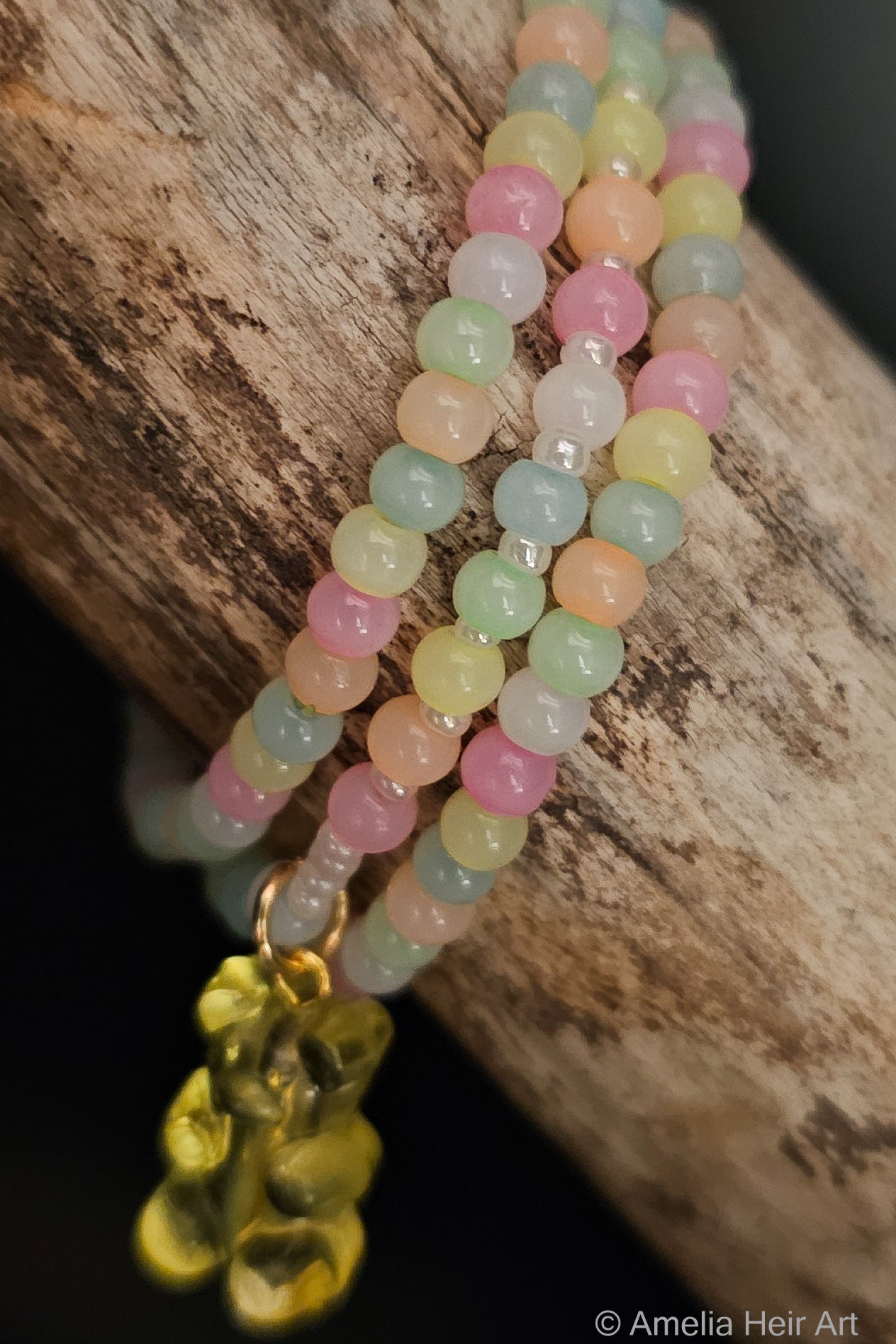 Pastel bead bracelet with a yellow gummy-bear charm on a wooden surface