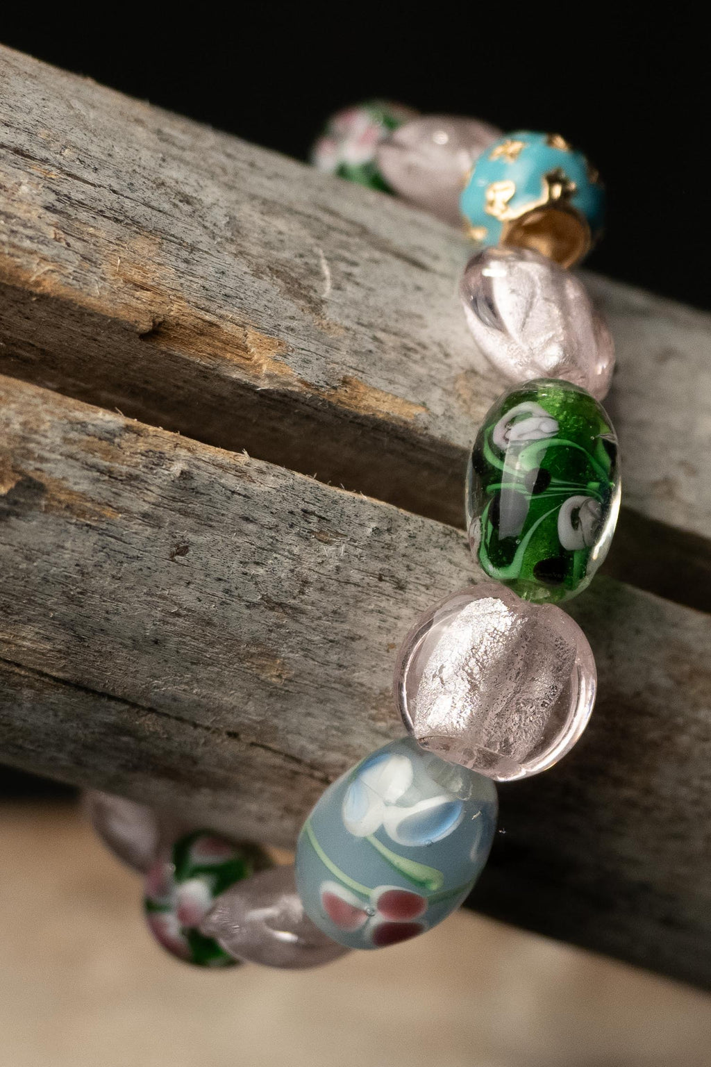 Amara handcrafted pink, green, blue & gold flower charm beaded bracelet on a wooden surface — Amelia Heir Art