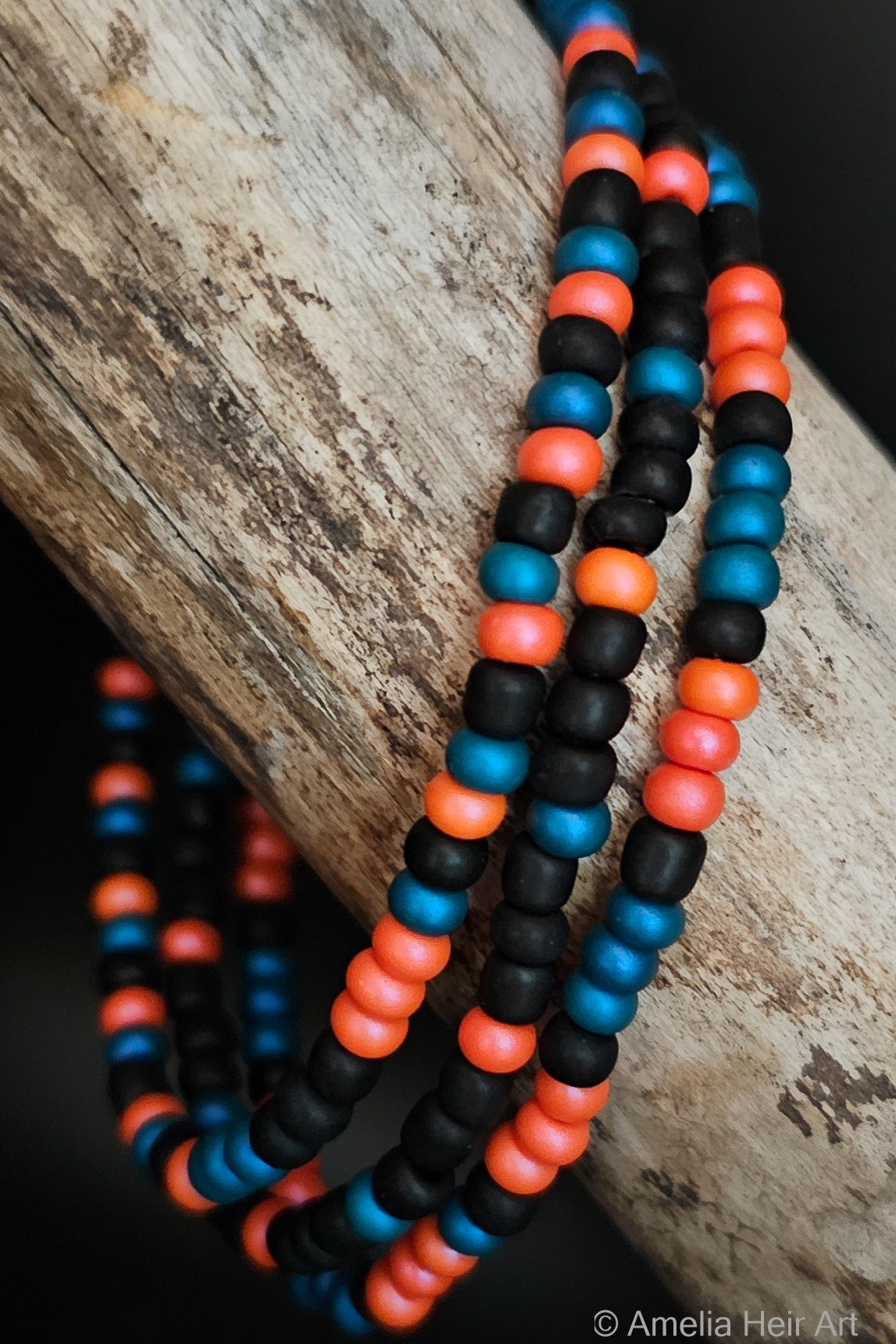 Three beaded bracelets in black, blue, and orange pink on a wooden surface.