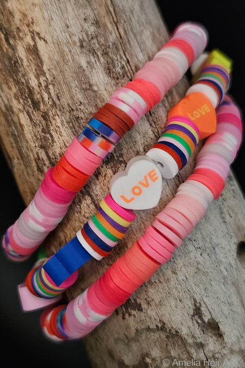 Colorful striped bracelets with 'LOVE' 
heart shaped beads on a wooden surface