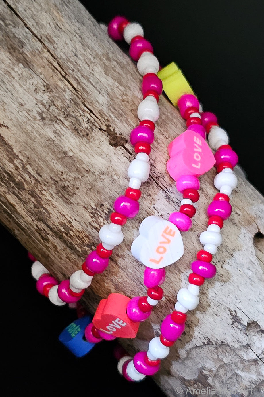 Colorful beaded bracelets with 'LOVE' heart-shaped charms on a wooden surface
