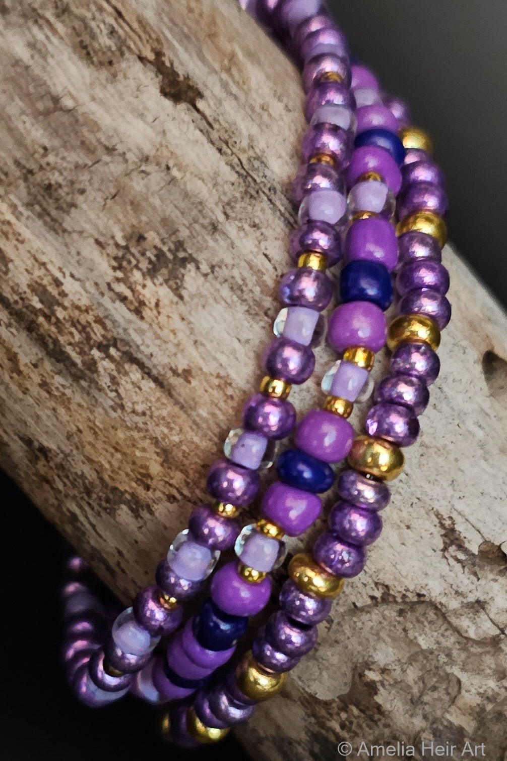 Three beaded bracelets in purple and gold on a textured wood surface.