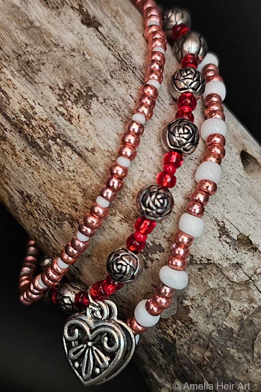 Pink and red beaded bracelets with silver rose beads and heart charms on a wooden surface