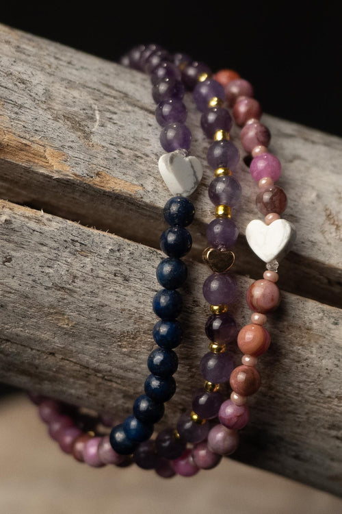 Three beaded bracelets with heart-shaped charms on a wooden surface