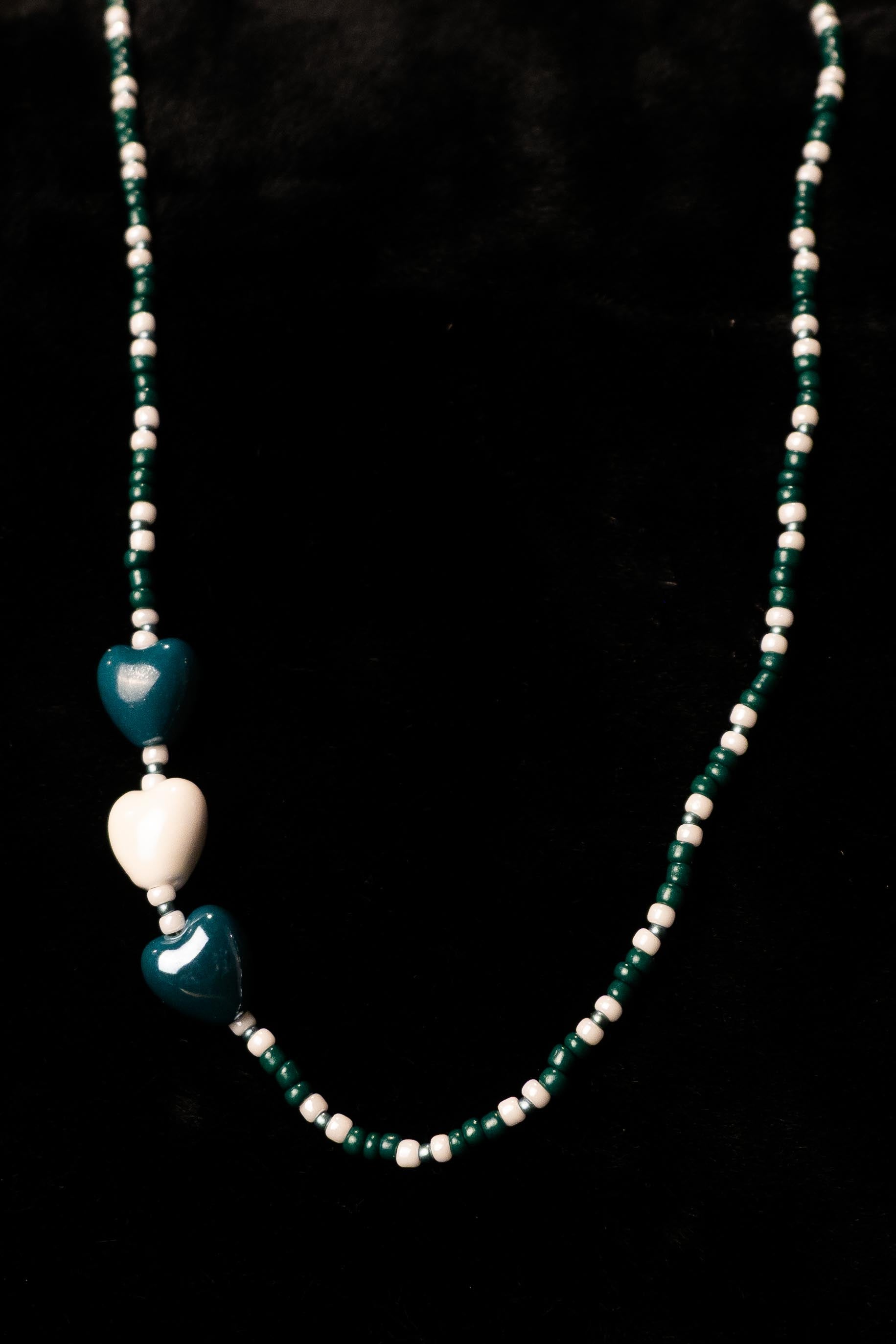 Forest green and white necklace with heart-shaped beads on a black background