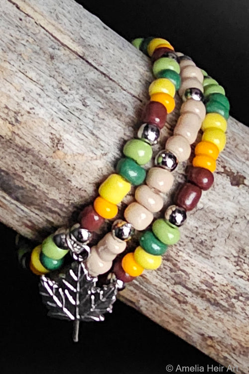 Beaded bracelets with colorful beads and silver accents with a silver leaf charm on a wooden surface