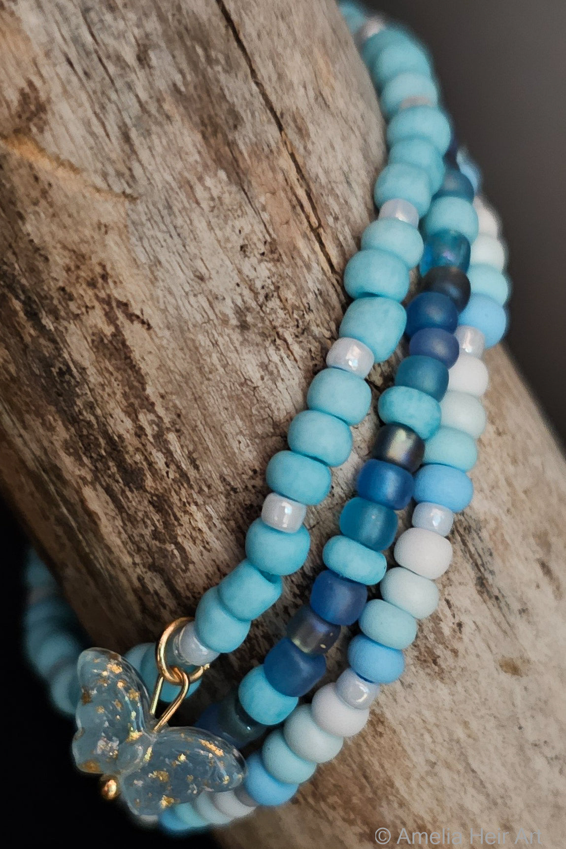 Stack of blue beaded bracelets with a butterfly charm on a wooden surface