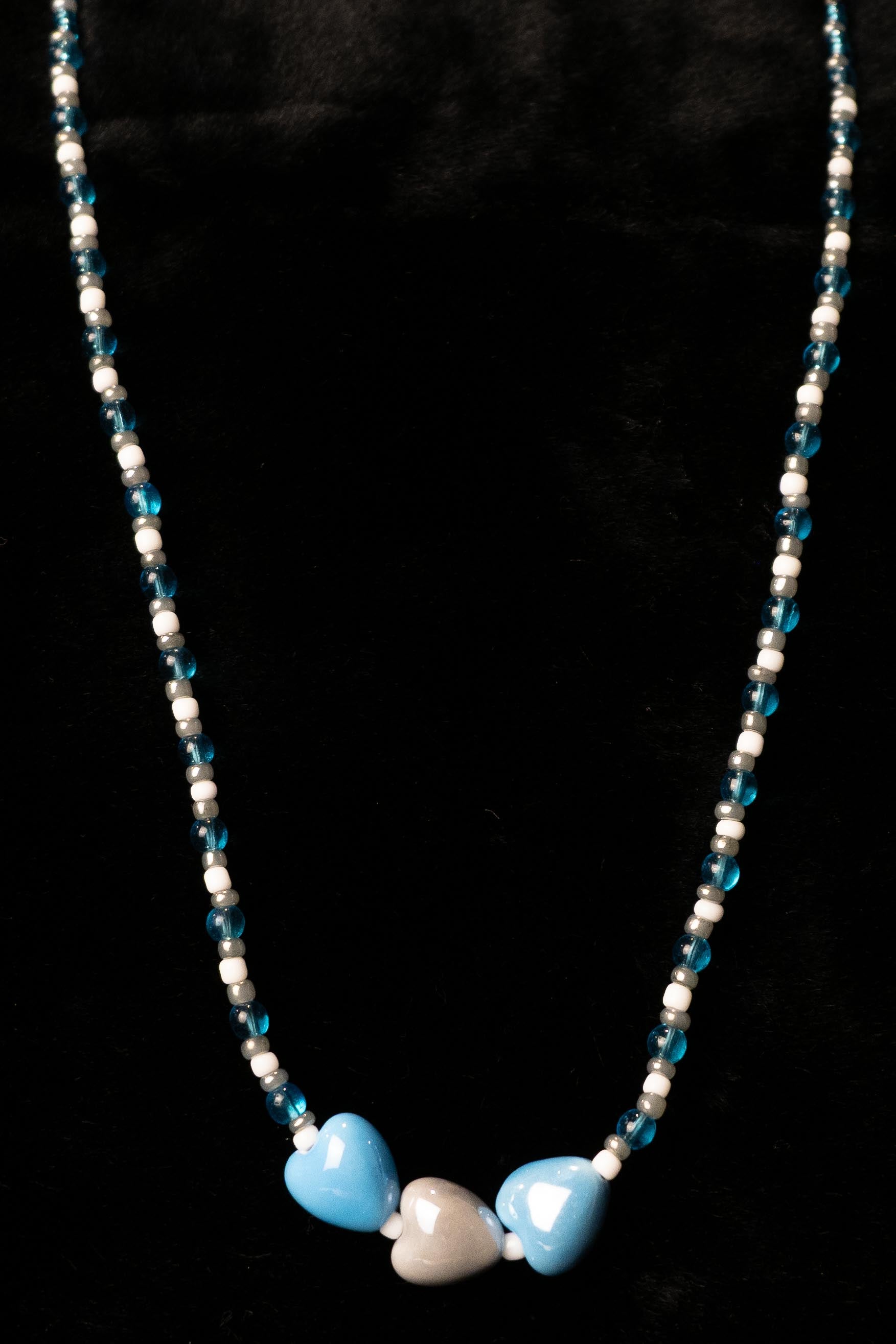 Necklace with blue, gray, and white heart-shaped beads on a black background
