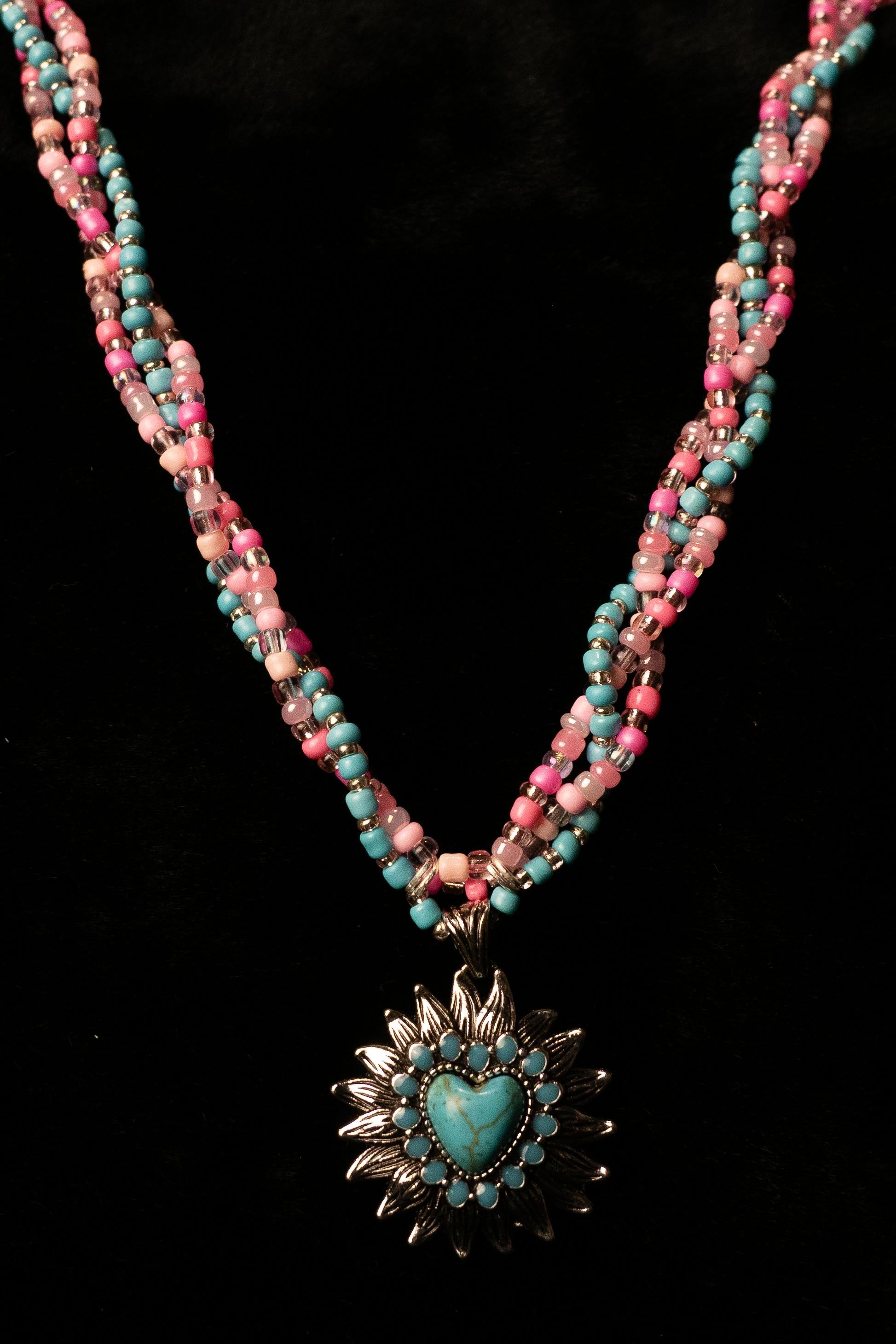 Necklace with pink and turquoise beads and a heart-shaped sunflower pendant on a black background