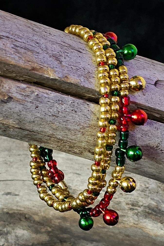 Beaded bracelet with gold, red, and green beads and tiny jingle bells on a wooden surface