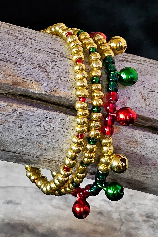 Three beaded bracelets in gold, green, and red with tiny jingle bells on a wooden surface.