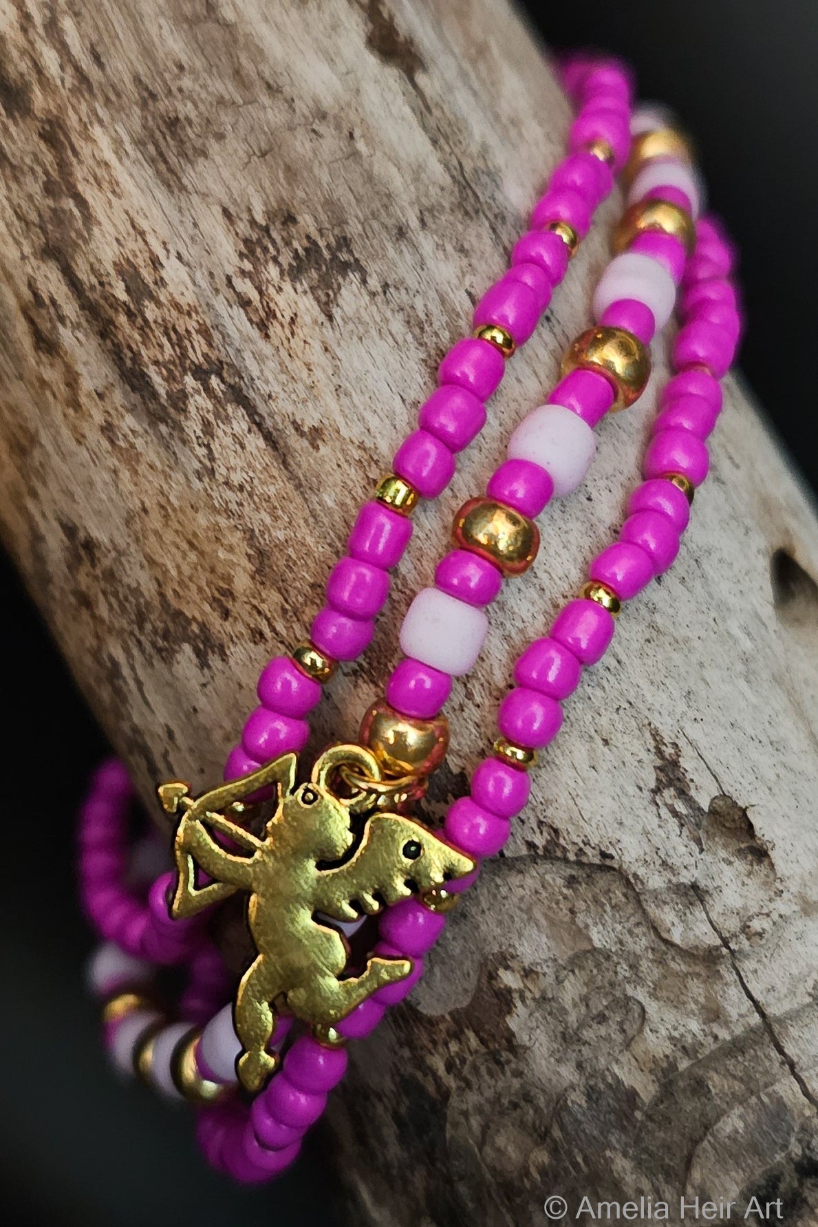 Three beaded bracelets with gold cupid charm on a wooden surface