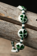 Bracelet with white beads featuring green clover patterns on a wooden surface