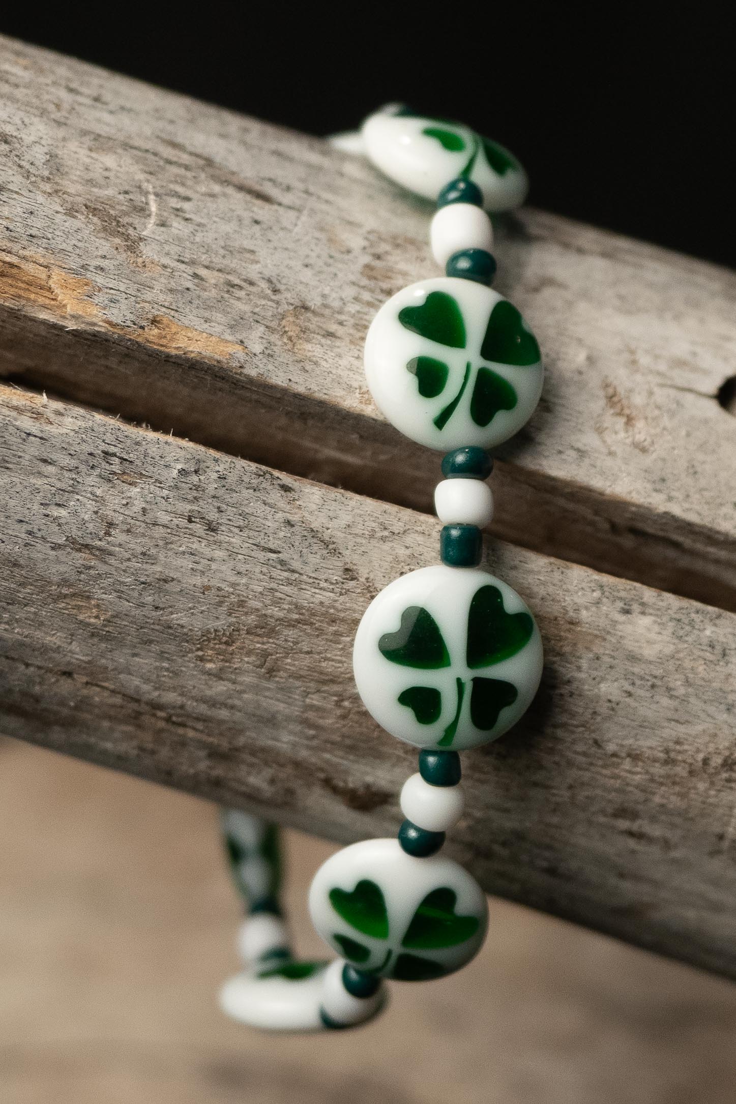 Bracelet with white beads featuring green clover patterns on a wooden surface
