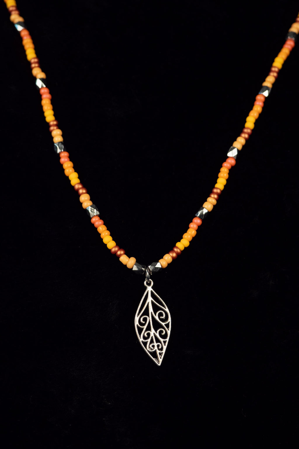Necklace with beads and a silver leaf pendant on a black background