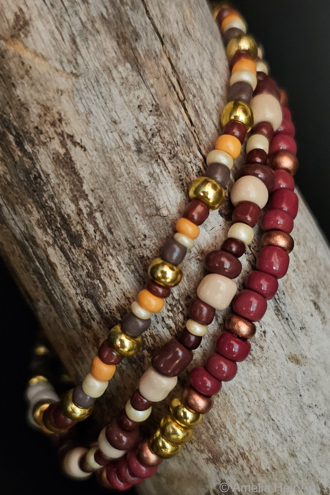 Three beaded bracelets in gray, yellow, gold, and brown on a wooden surface
