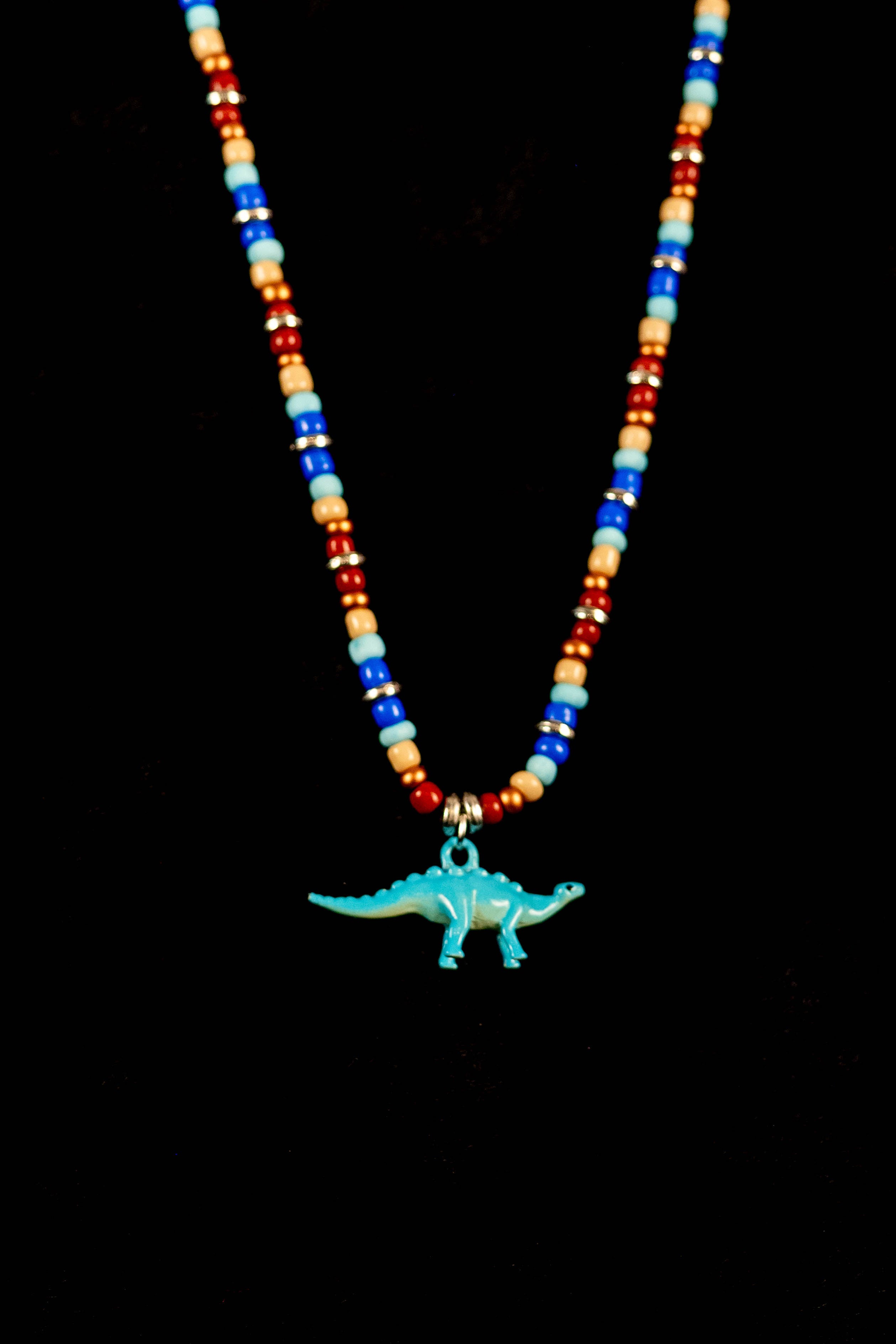 Necklace with colorful beads and a blue dinosaur pendant on a black background