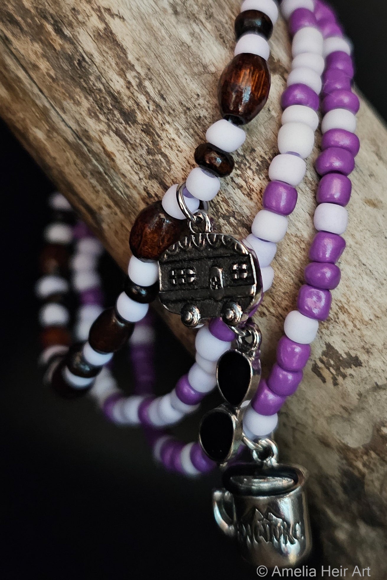 Purple and brown beaded bracelets with SILVER camping trailer, sunglasses, and 'ADVENTURE' MUG charms on a wooden surface