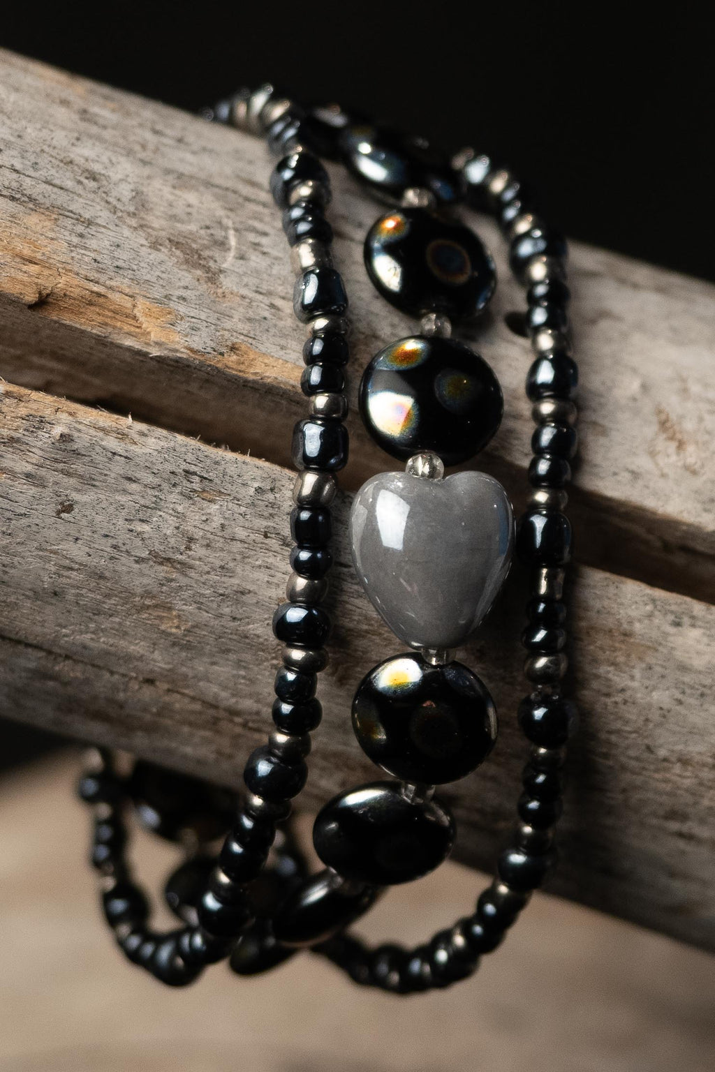 Beaded necklace with black and gray beads and a heart accent on a wooden surface