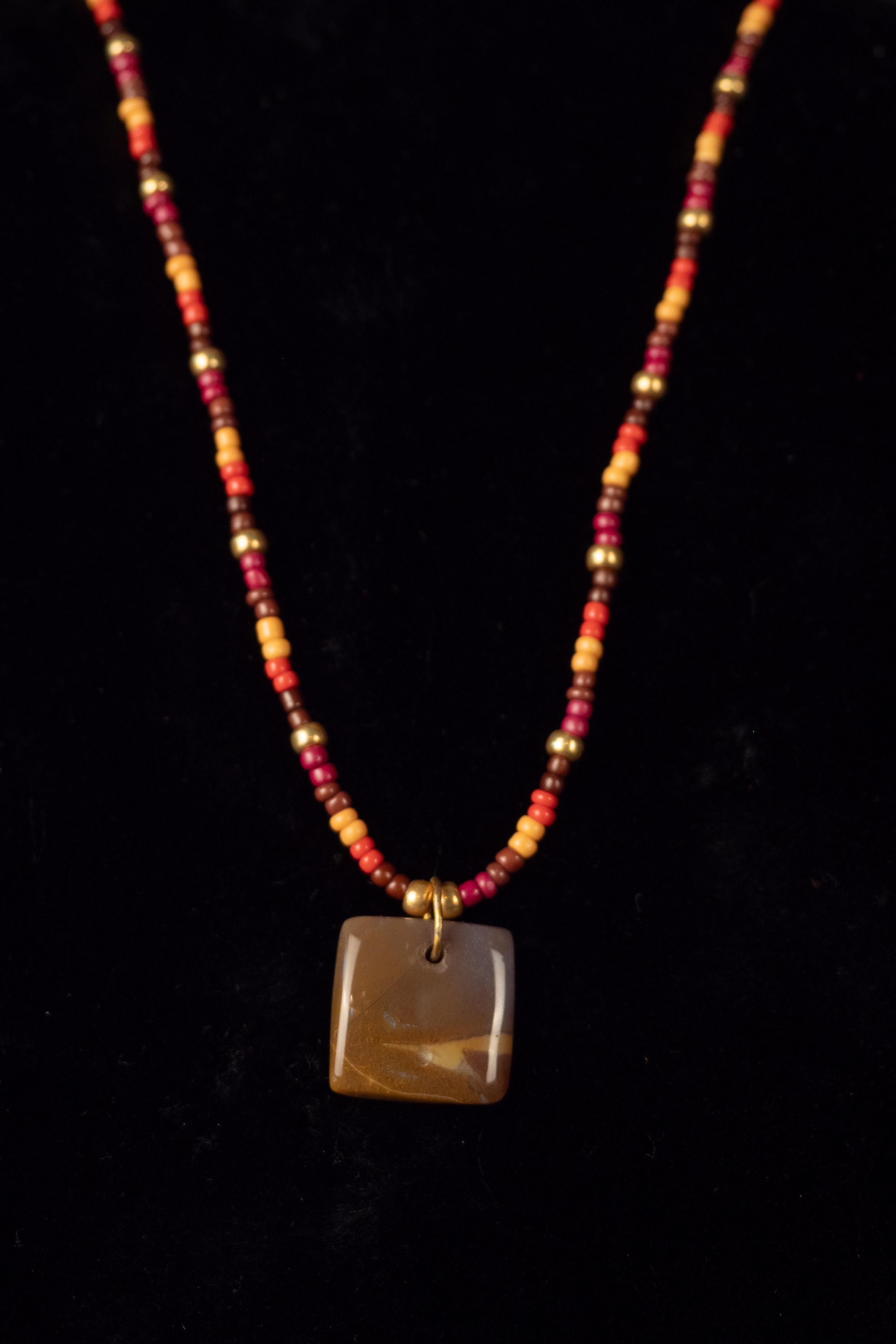 Necklace with a brown square stone pendant and multicolored beads on a black background