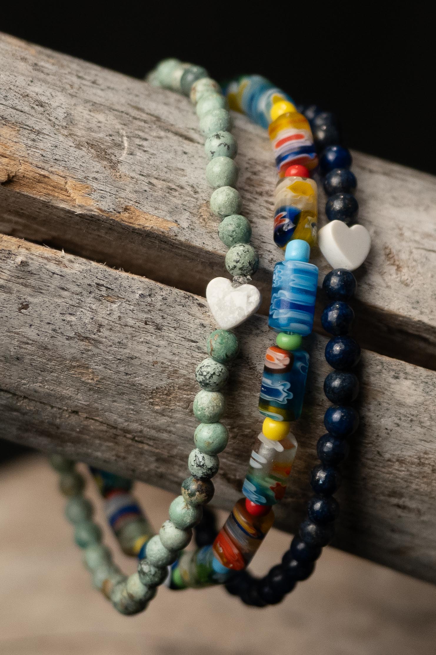 Colorful beaded bracelets with white heart-shaped beads on a wooden surface