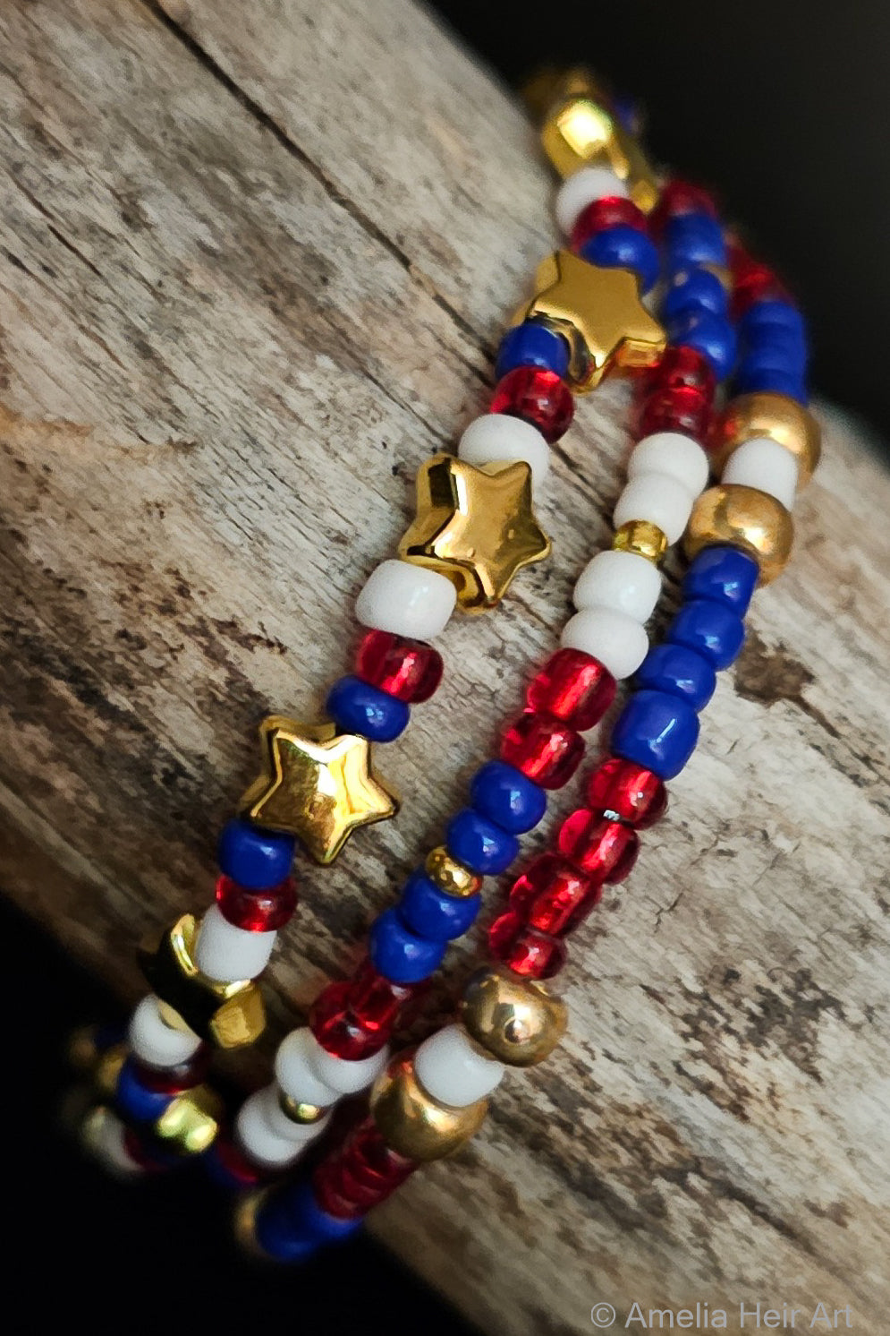 Stack of beaded bracelets with red, white, blue, and gold beads with gold star accents on a wooden surface.