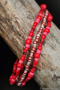 Three beaded bracelets in red, pink, and white on a wooden surface.