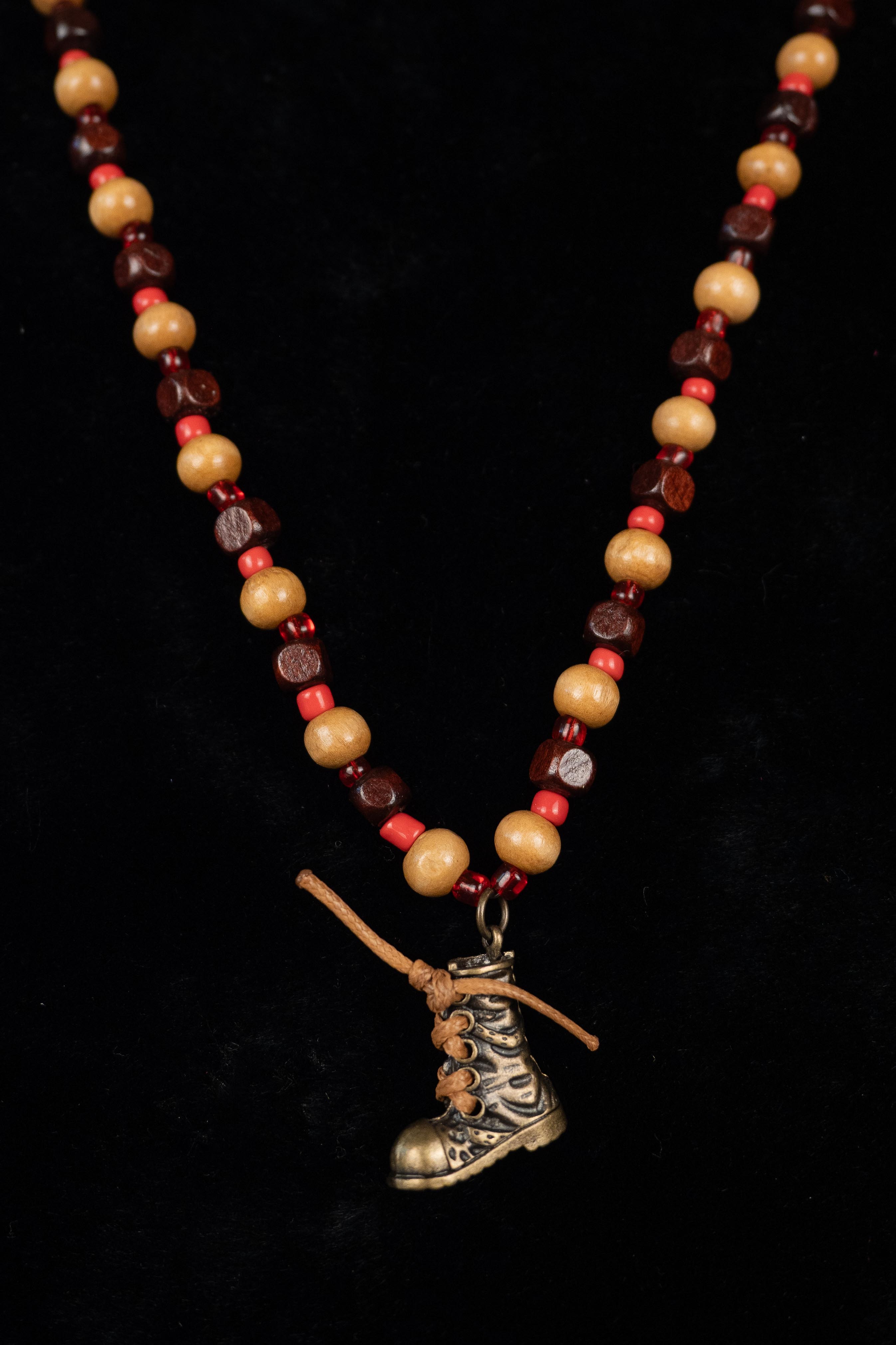 Necklace with wood beaded chain and hiking boot charm on a black background