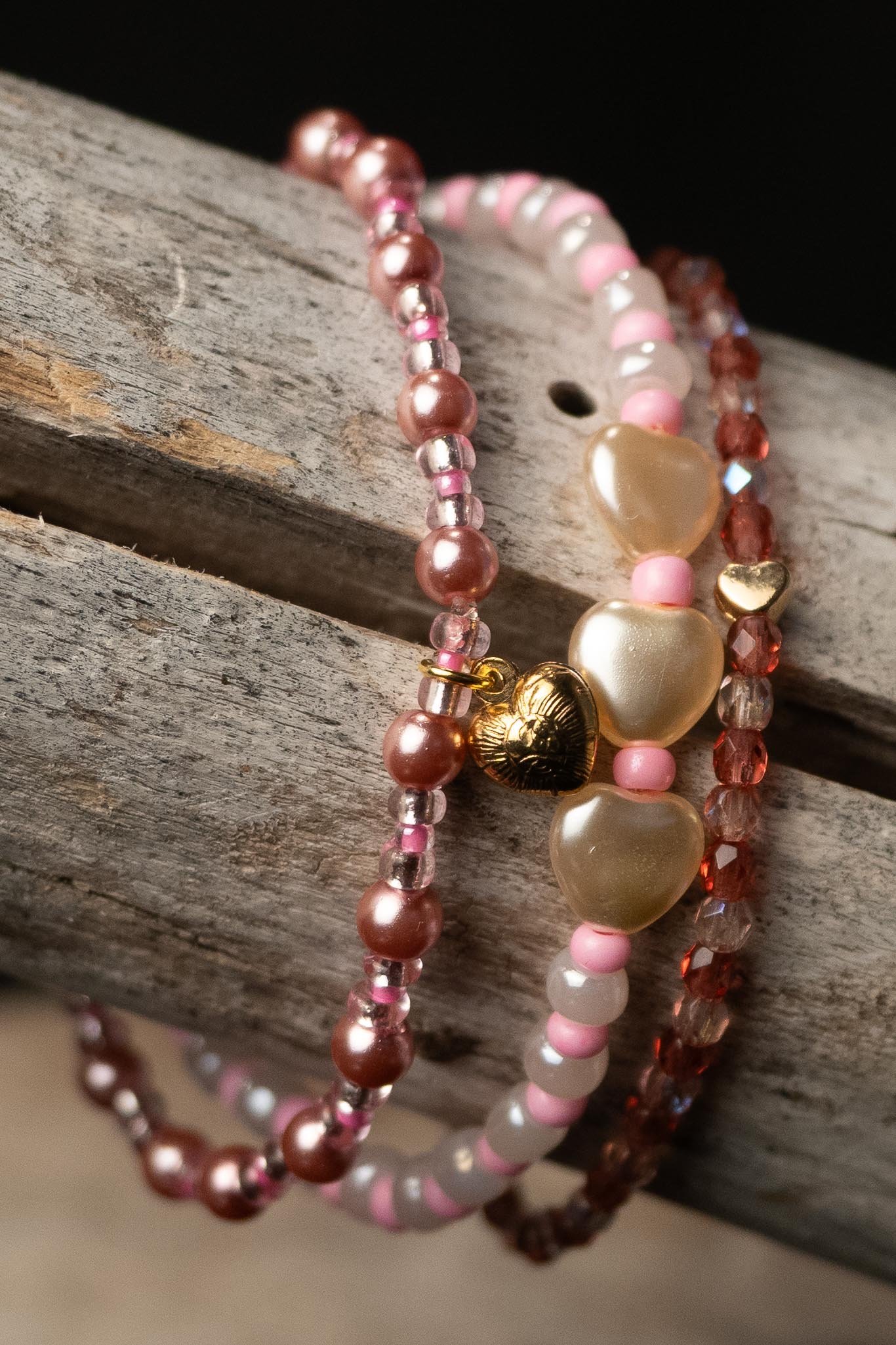 Stack of pink and white beaded bracelets with heart-shaped beads and a tiny gold heart charm on a wooden surface