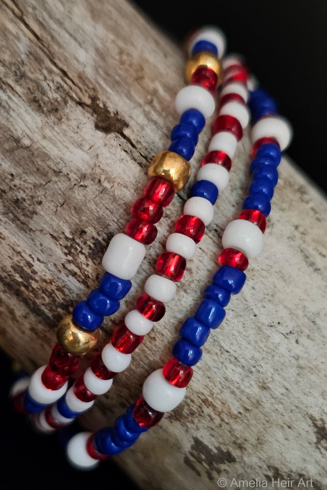 Three beaded bracelets in red, gold, white, and blue on a wooden surface.