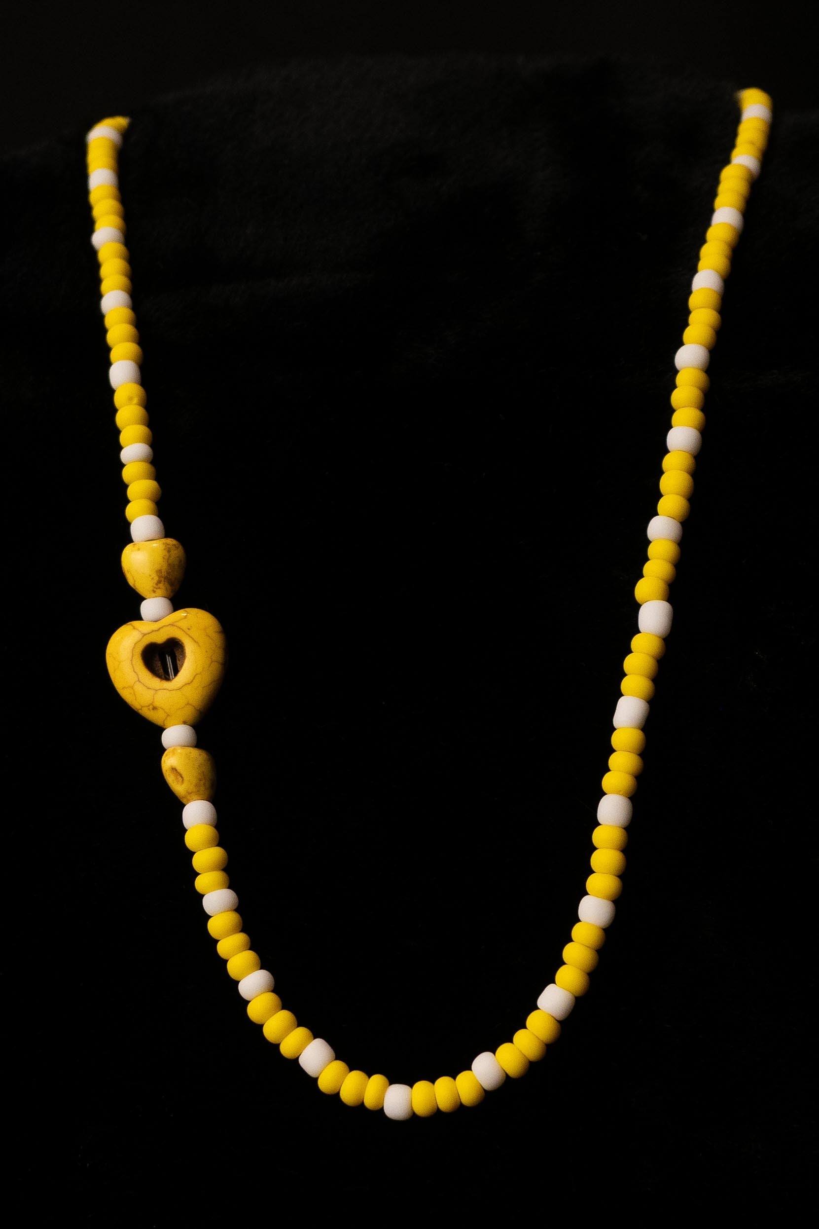 Necklace with yellow and white beads with heart-shaped bead accents on a black background