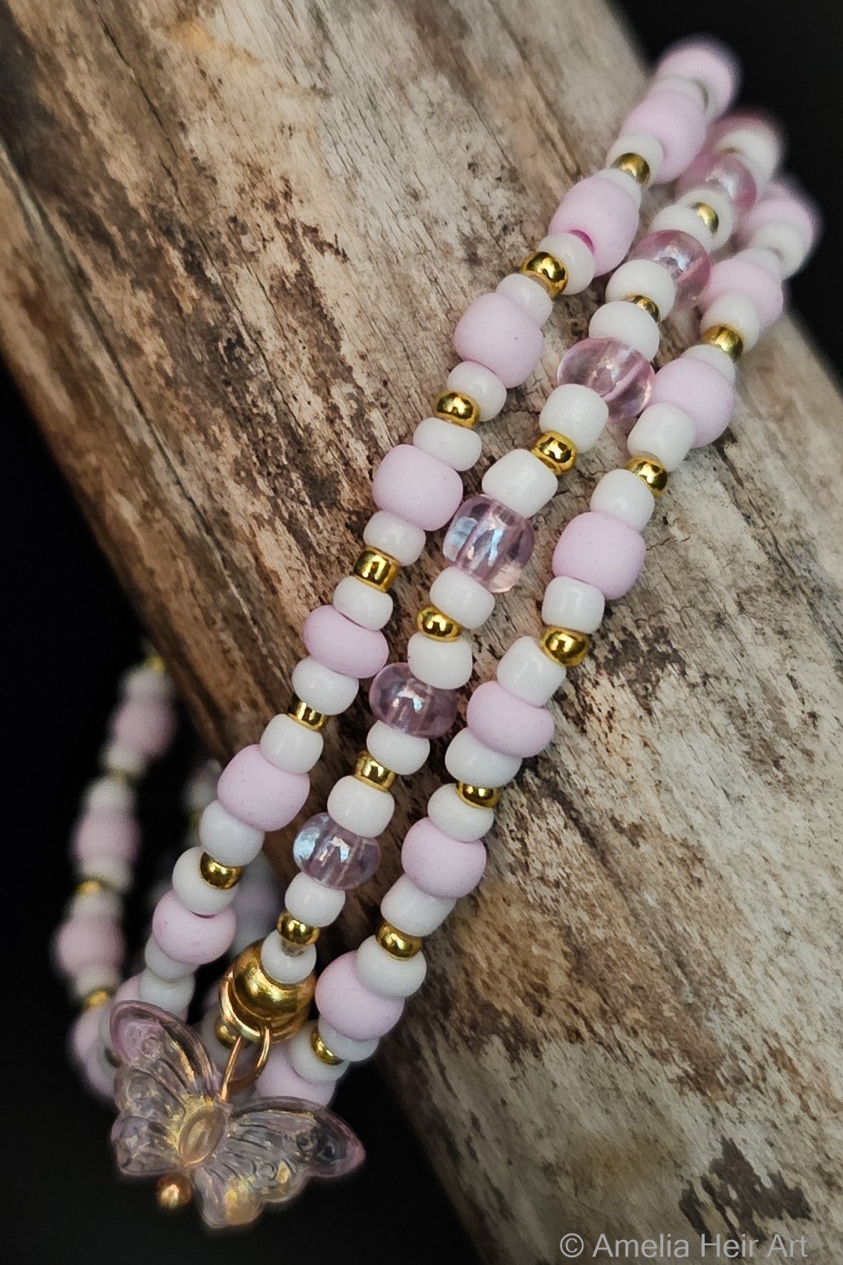 Set of beaded bracelets with pink, white, and gold beads with a translucent butterfly charm on a wooden surface.