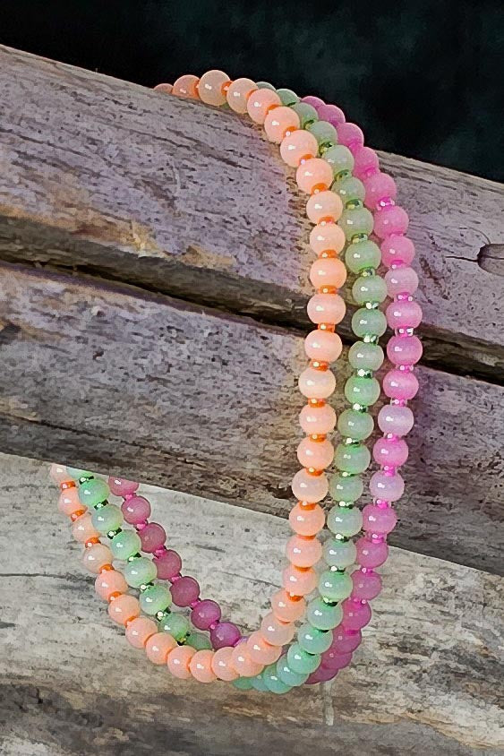 Stack of orange, green, and pink beaded bracelets on a wooden surface