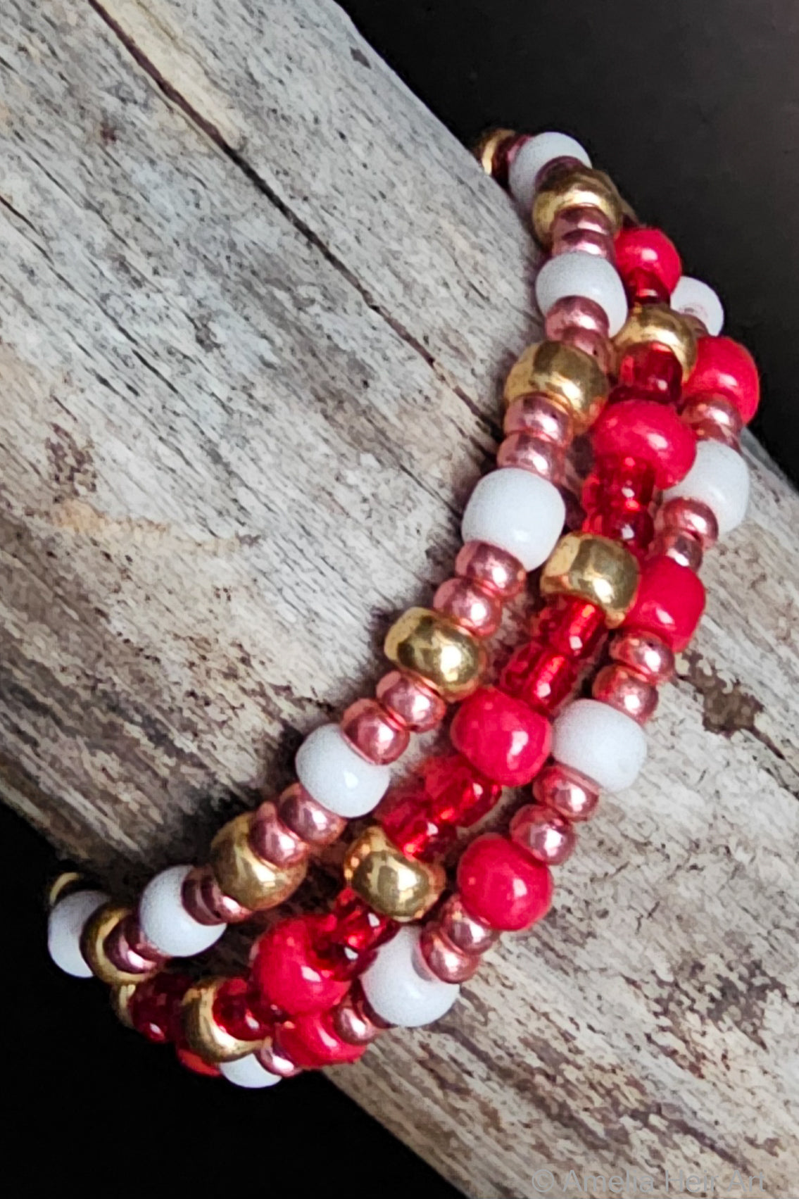 Stack of red, pink, white, and gold beaded bracelets on a wooden surface