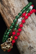 Three beaded bracelets in green, red, white and gold on a wooden surface.