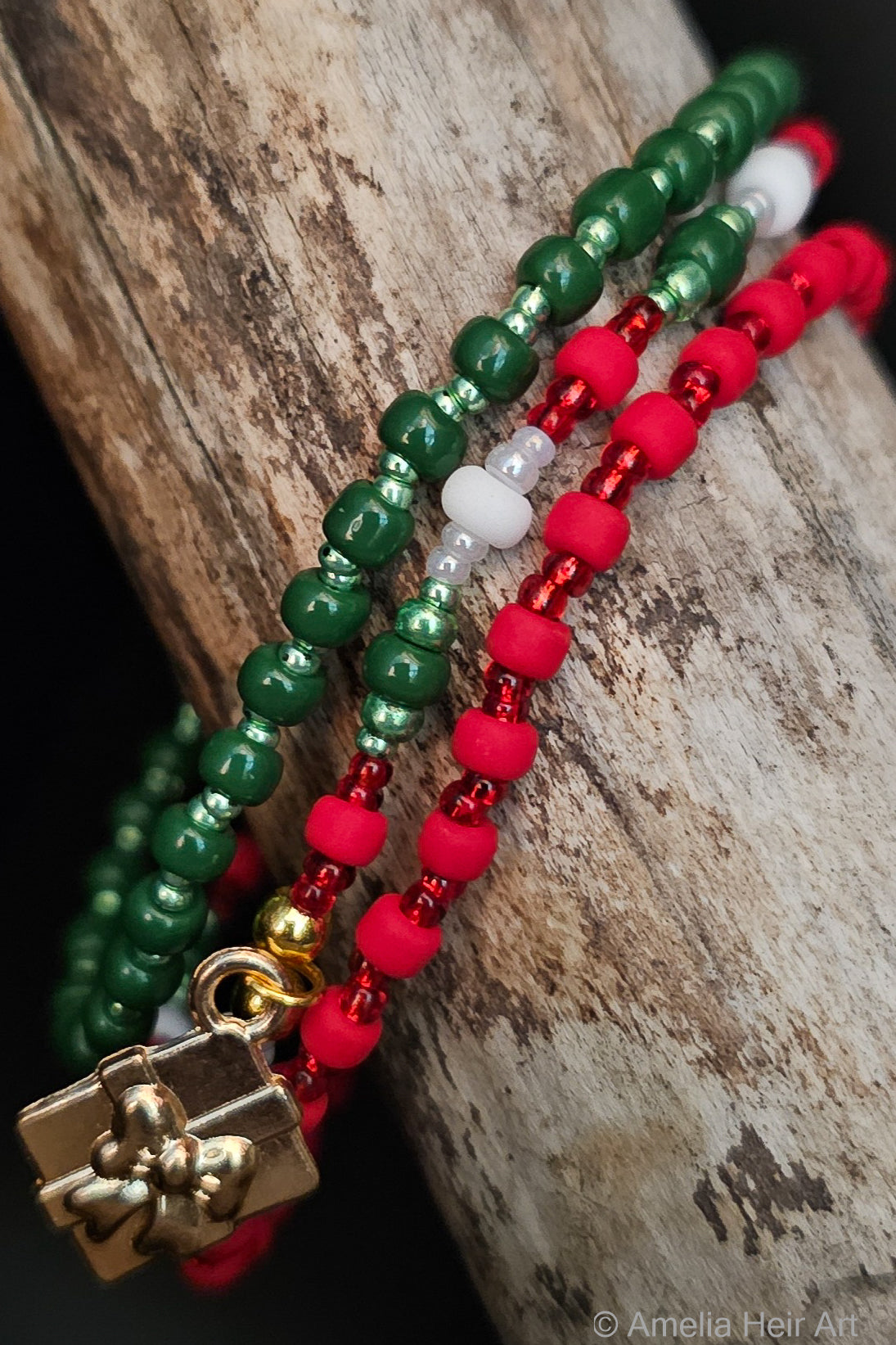 Three beaded bracelets in green, red, white and gold on a wooden surface.