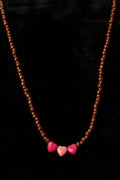 Necklace with brown beads and pink heart-shaped beads on a black background