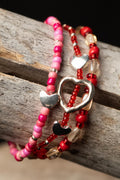 Pink, red, and clear beaded bracelets with silver heart charms on a wooden surface