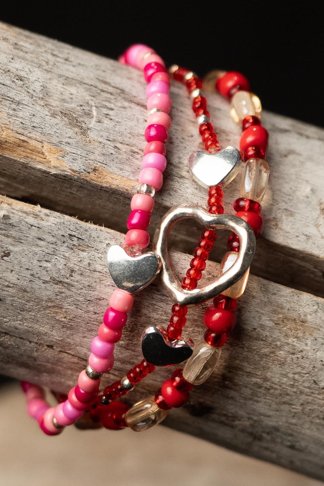 Pink, red, and clear beaded bracelets with silver heart charms on a wooden surface